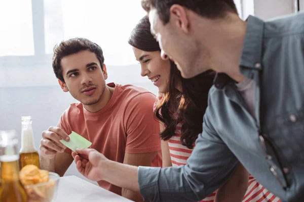 Homem sério tomar nota pegajosa ao jogar jogo de nome com amigos sorridentes — Stock Photo