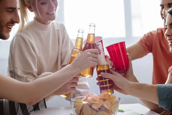Vista cortada de amigos felizes batendo garrafas de cerveja e copos de plástico com refrigerante — Fotografia de Stock