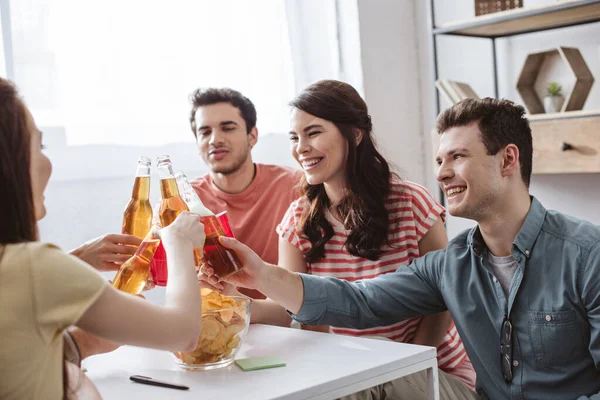 Glückliche Freunde klirren mit Flaschen und Tassen beim Namensspiel zu Hause — Stockfoto