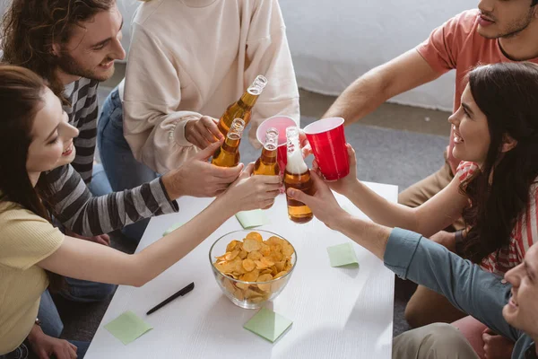 Vista de ángulo alto de amigos felices tintineo con botellas y tazas mientras juega juego de nombre en casa - foto de stock
