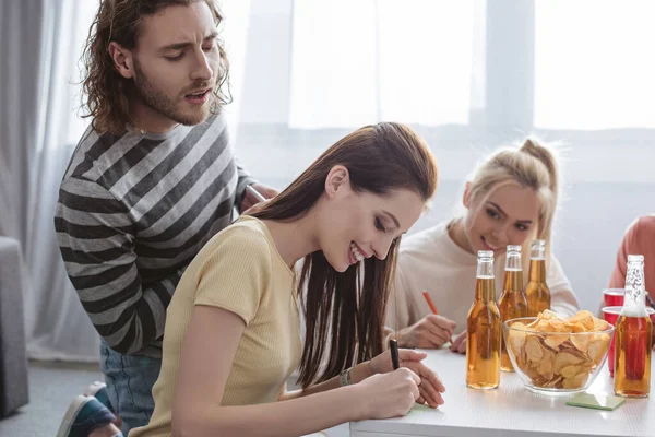 Curieux homme regardant fille écriture sur note collante tout en jouant jeu de nom avec des amis — Photo de stock