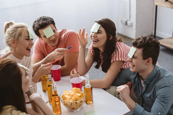 Cheerful man and woman pointing with pens while playing name game with friends — Stock Photo