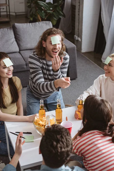 Vista de ángulo alto de hombre alegre señalando con el dedo mientras juega juego de nombre con amigos - foto de stock