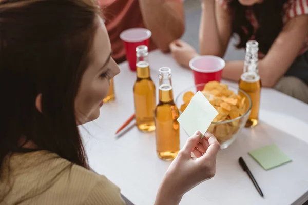 Enfoque selectivo de niña sosteniendo nota pegajosa mientras juega juego de nombre con amigos - foto de stock