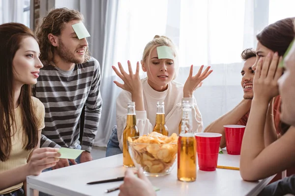 Chica confundida mostrando gesto de encogimiento mientras juega juego de nombre con amigos - foto de stock