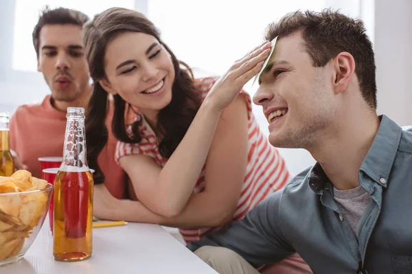 Chica feliz poner nota pegajosa en la frente del hombre sonriente mientras juega nombre juego - foto de stock