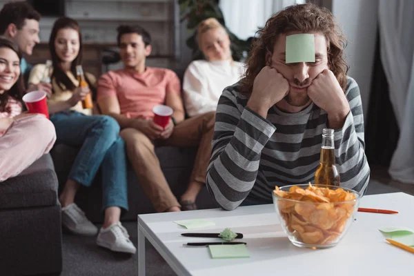 Selective focus of bored man with sticky note on forehead playing name game with friends — Stock Photo