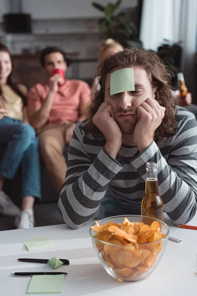 Selective focus of bored man with sticky note on forehead playing name game with friends — Stock Photo