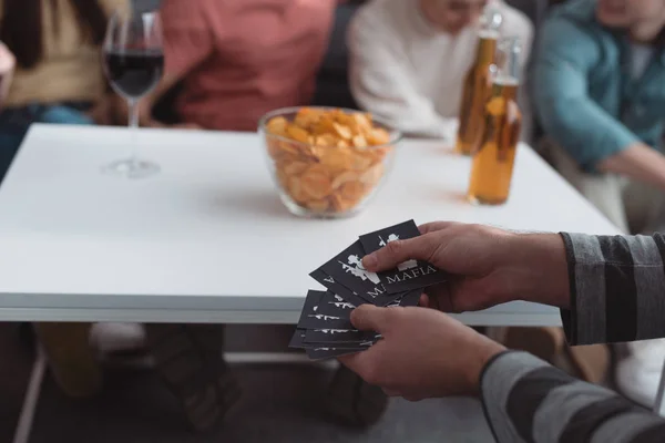 KYIV, UKRAINE - JANUARY 27, 2020: partial view of man holding mafia game cards near table with chips and drinks — Stock Photo