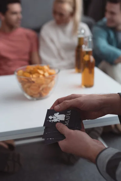 QUIIV, UCRÂNIA - JANEIRO 27, 2020: visão recortada do homem segurando cartas de jogo da máfia perto da mesa com batatas fritas e cerveja — Fotografia de Stock