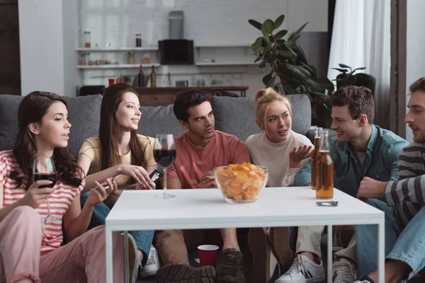 KYIV, UKRAINE - JANUARY 27, 2020: thoughtful friends playing mafia game while sitting near table with chips and drinks — Stock Photo