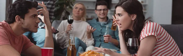 Plano panorámico de chica y chico peleando mientras amigos sentados en el sofá y beber bebidas - foto de stock