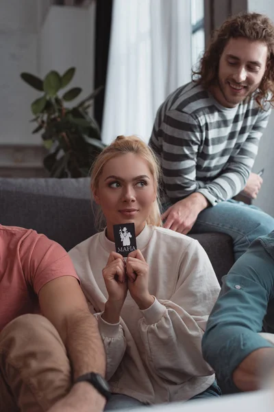 QUIIV, UCRÂNIA - JANEIRO 27, 2020: menina sorridente segurando cartão enquanto joga jogo de máfia com amigos — Fotografia de Stock