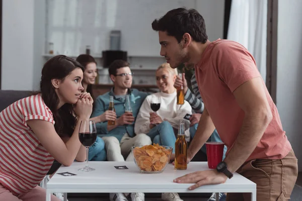 Selective focus of displeased girl and guy looking at each other while friends resting on sofa — Stock Photo