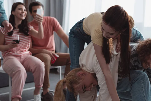 Smiling girl taking photo of cheerful friends playing fun game at home — Stock Photo