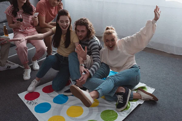 KYIV, UKRAINE - JANUARY 27, 2020: high angle view of friends sitting on twister game mat while others resting on sofa — Stock Photo