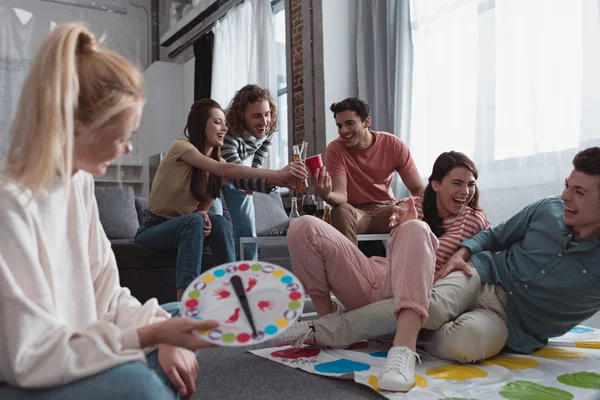 KYIV, UCRANIA - 27 de enero de 2020: enfoque selectivo de la niña sosteniendo mueve el tablero mientras sus amigos alegres juegan al twister game - foto de stock