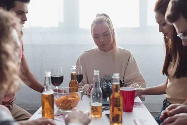 KYIV, UKRAINE - JANEIRO 27, 2020: amigos alegres que jogam loteria enquanto se sentam à mesa com bebidas e batatas fritas — Fotografia de Stock