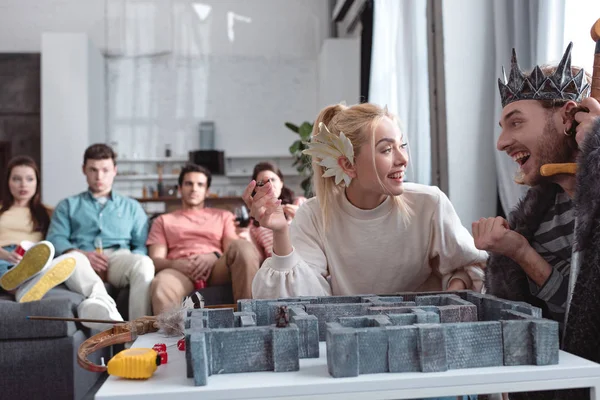 KYIV, UKRAINE - JANUARY 27, 2020: selective focus of cheerful girl and guy in fairy costumes playing labyrinth game near bored friends sitting on sofa — Stock Photo