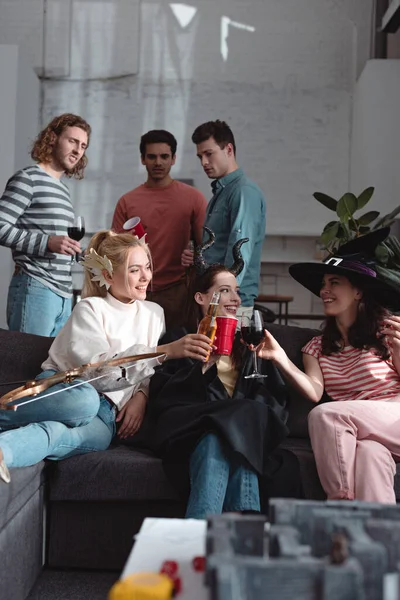 KYIV, UKRAINE - JANUARY 27, 2020: selective focus of cheerful girl drinking beverages whille sitting on sofa near labyrinth board while friends standing on background — Stock Photo