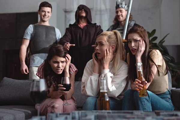 Schockierte Mädchen, die Bier und Wein trinken, während Männer in Märchenkostümen im Hintergrund stehen — Stockfoto