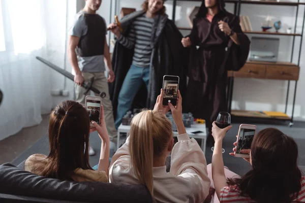 Vista posterior de las niñas tomando fotos de los hombres jóvenes en trajes de hadas en los teléfonos inteligentes - foto de stock