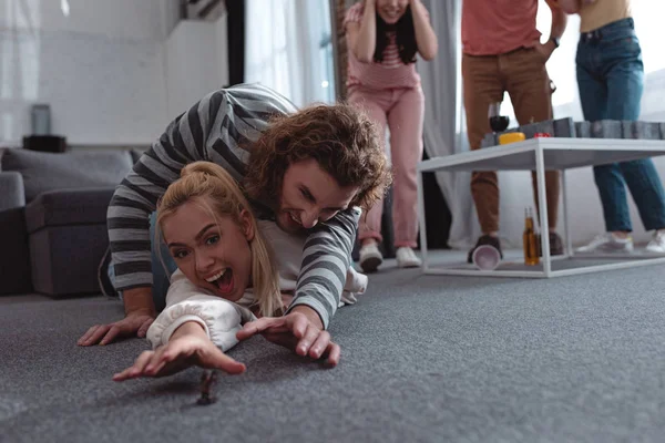 Aufgeregtes Mädchen und Mann, das auf dem Boden liegt und versucht, Spielzeugfigur in die Nähe von Freunden zu nehmen, die im Hintergrund stehen — Stockfoto