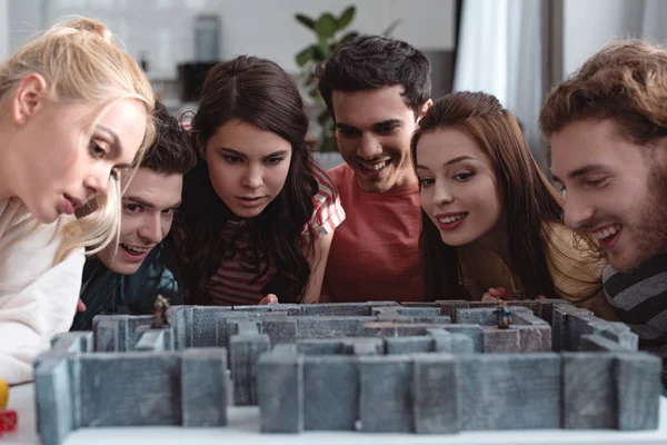 KYIV, UKRAINE - JANUARY 27, 2020: smiling and thoughtful friends looking at labyrinth board game on table — Stock Photo
