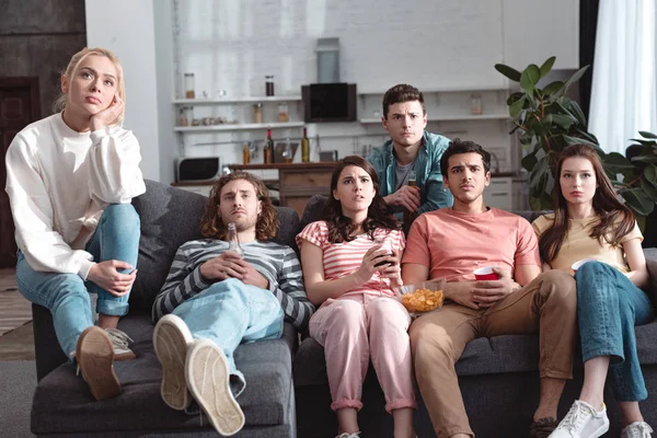 Attentive friends watching tv while sitting on sofa at home — Stock Photo