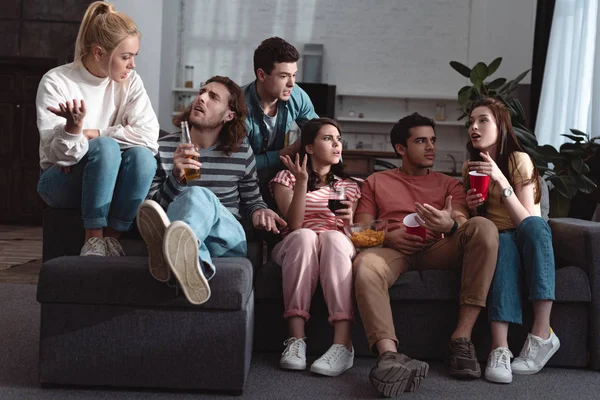 Jóvenes amigos hablando y haciendo gestos mientras están sentados en el sofá en casa - foto de stock