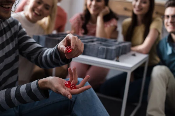 KYIV, UCRANIA - 27 de enero de 2020: enfoque selectivo del tipo que sostiene dados cerca de amigos sentados cerca del laberinto juego de mesa - foto de stock