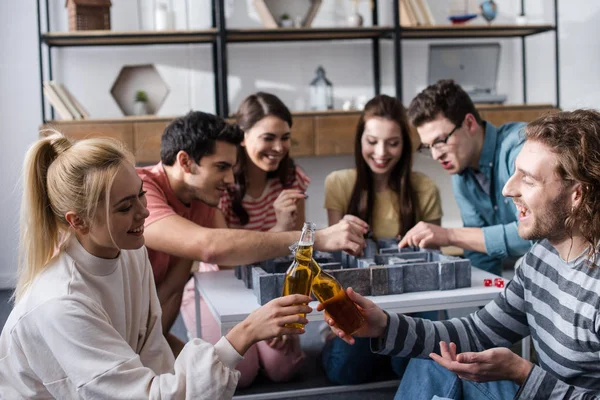 KYIV, UCRAINA - GENNAIO 27, 2020: ragazza allegra e ragazzo che si stringe le bottiglie di birra vicino agli amici giocando al gioco del labirinto — Stock Photo