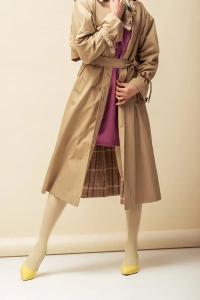 Обрізаний вид афроамериканської дівчини в траншеї пальто, що стоїть на бежевому — стокове фото