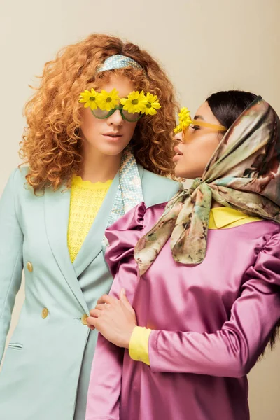 Afro-américaine fille et rousse femme dans des lunettes de soleil avec des fleurs isolées sur beige — Photo de stock