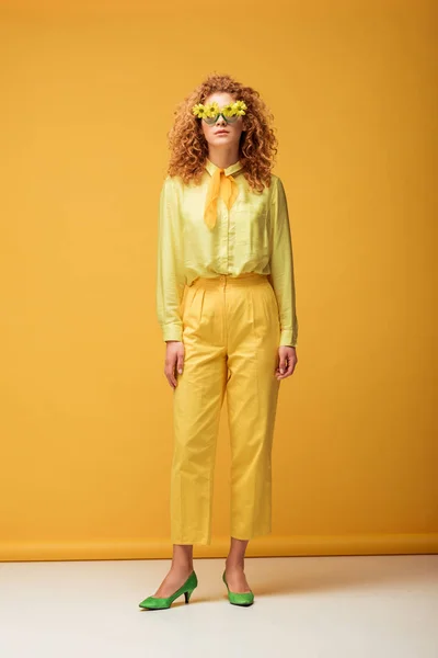 Rousse bouclée femme en lunettes de soleil avec des fleurs posant sur jaune — Photo de stock