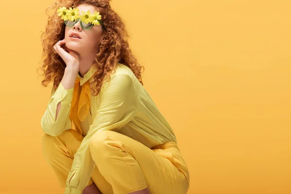 Стильна руда жінка в сонцезахисних окулярах з квітами, сидячи ізольовано на жовтому — Stock Photo