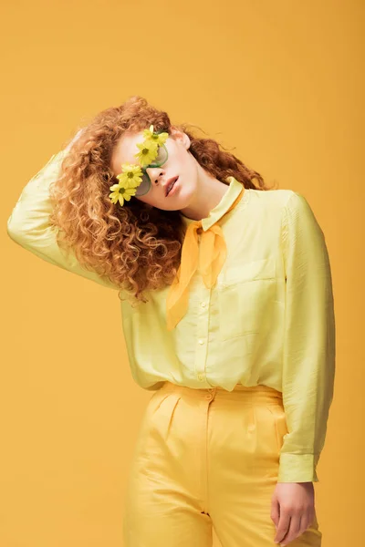 Stylish redhead woman in sunglasses with flowers posing isolated on yellow — Stock Photo
