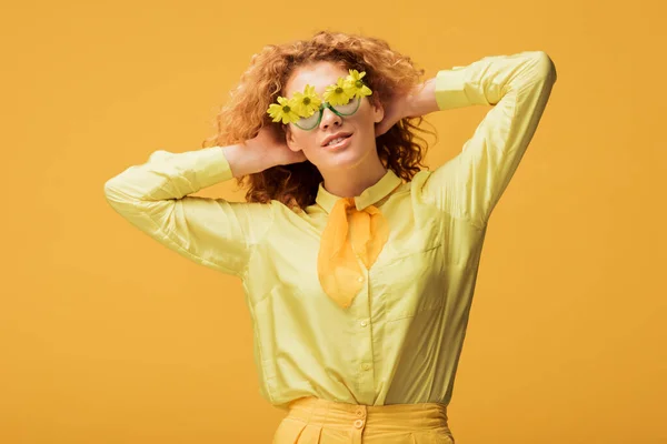 Femme rousse à la mode dans des lunettes de soleil avec des fleurs posant isolé sur jaune — Photo de stock