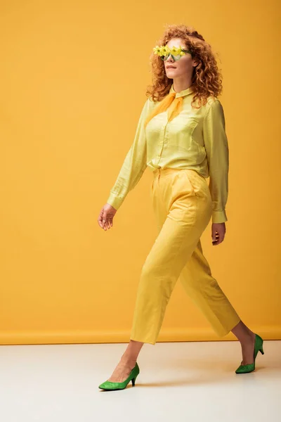 Elegante donna rossa in occhiali da sole con fiori che camminano sul giallo — Foto stock