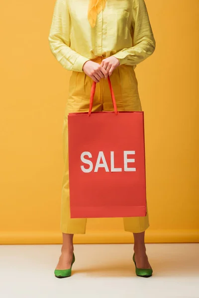 Vista recortada de la mujer joven sosteniendo bolsa de compras con letras venta mientras está de pie en amarillo - foto de stock