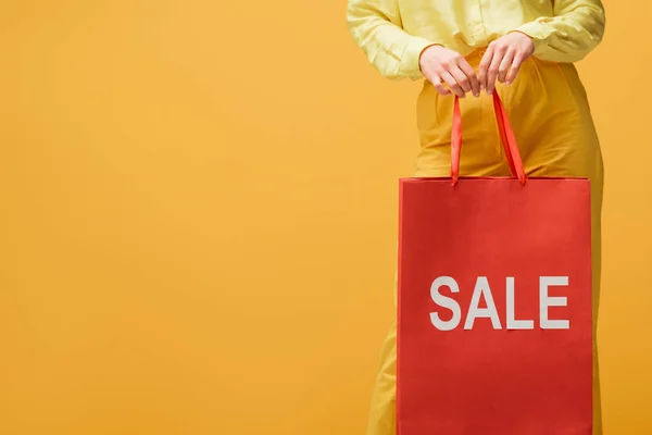 Vista recortada de la mujer joven sosteniendo bolsa de compras con letras venta mientras está de pie aislado en amarillo - foto de stock