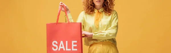 Plano panorámico de mujer pelirroja elegante sosteniendo bolsa de compras con letras venta aislado en amarillo - foto de stock