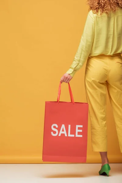 Vue arrière de femme rousse élégant tenant sac à provisions avec lettrage de vente sur jaune — Photo de stock