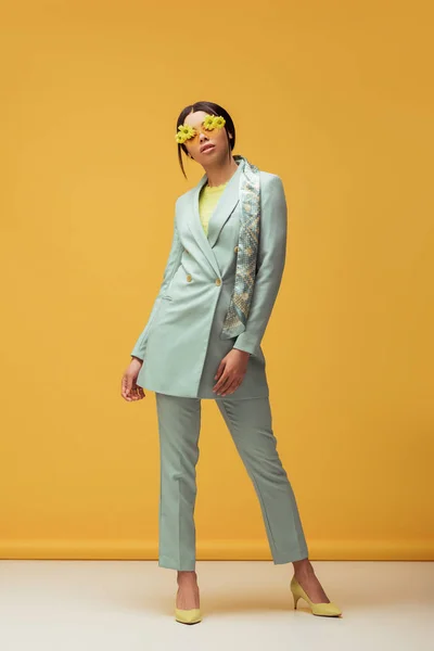 Ragazza afroamericana alla moda in abito, sciarpa e occhiali da sole con fiori in posa su giallo — Foto stock
