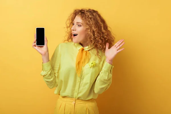 Aufgeregte rothaarige Frau blickt auf Smartphone mit leerem Bildschirm auf Gelb — Stockfoto