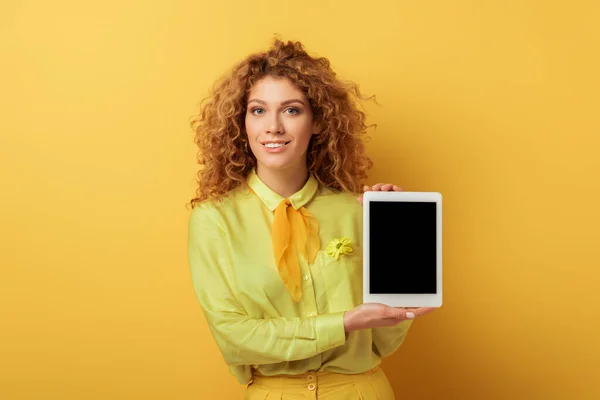 Mujer pelirroja feliz sosteniendo tableta digital con pantalla en blanco aislado en amarillo - foto de stock