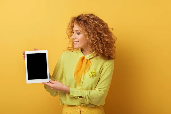 Cheerful redhead woman holding digital tablet with blank screen isolated on yellow — Stock Photo