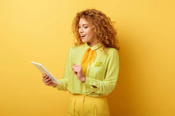 Щаслива руда дівчина дивиться на цифровий планшет на жовтому — стокове фото