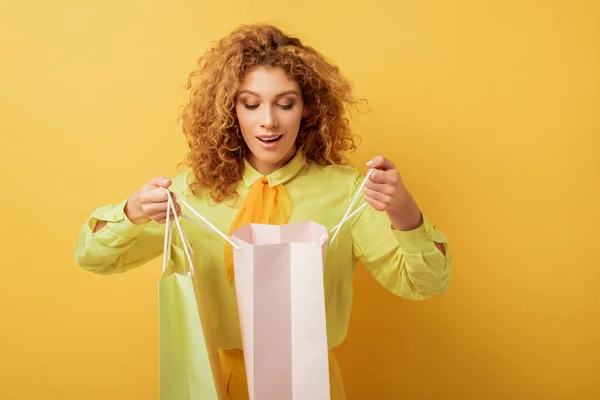 Chica pelirroja emocionada mirando el bolso de compras en amarillo - foto de stock