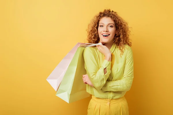 Femme coûteuse et bouclée tenant des sacs à provisions sur jaune — Photo de stock